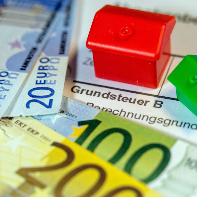 Ein Spielzeughaus und die Nachbildung von Euro-Geldscheinen liegen auf einem Abgabenbescheid für die Entrichtung der Grundsteuer.&nbsp;