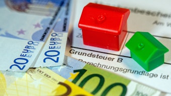 Ein Spielzeughaus und die Nachbildung von Euro-Geldscheinen liegen auf einem Abgabenbescheid für die Entrichtung der Grundsteuer.