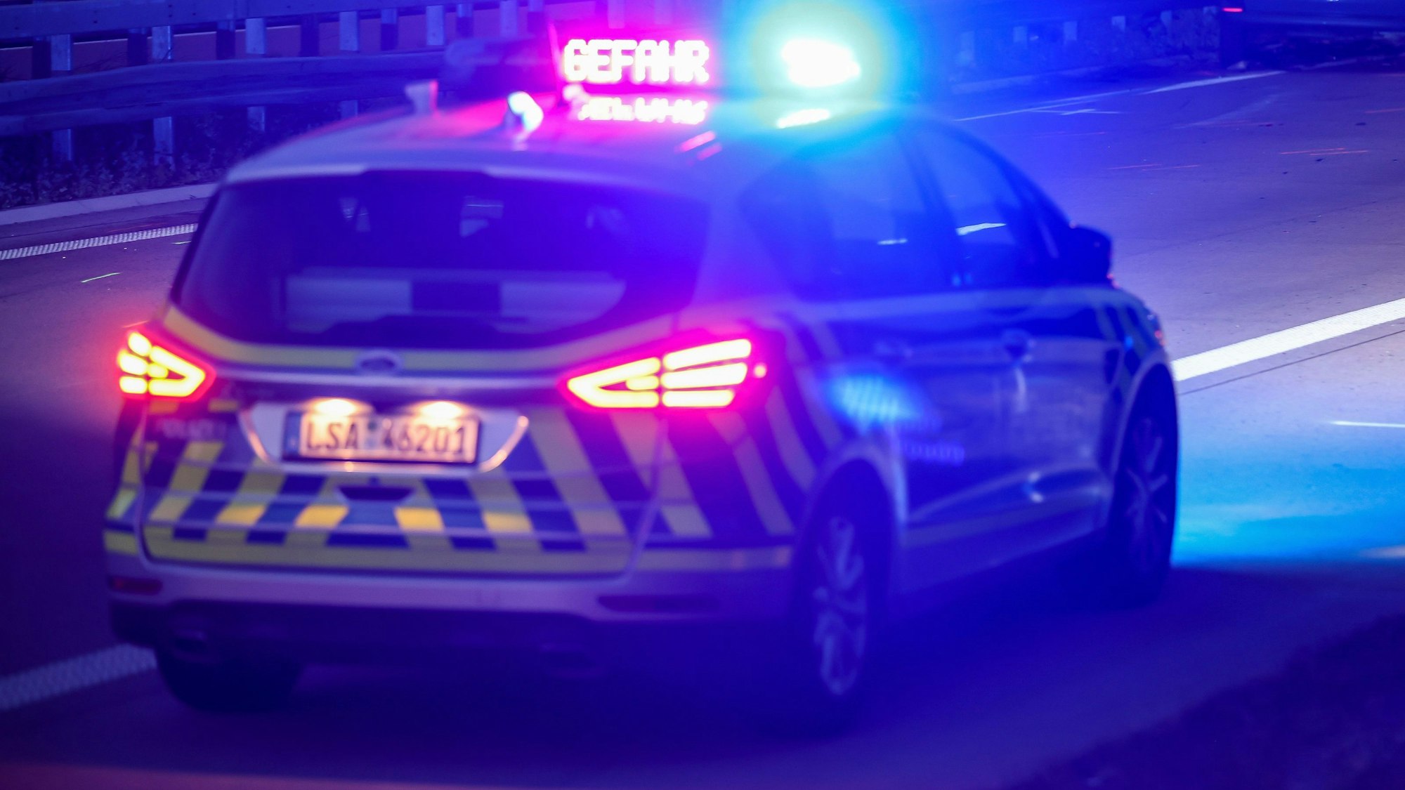 Mit Blaulicht und der Anzeige „Gefahr“ steht ein Polizeifahrzeug nach einem schweren Verkehrsunfall auf der Autobahn.