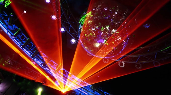 Eine tolle Lasershow in der Disco: Orangefarbene Lichter strahlen eine Discokugel an und sorgen damit für Partystimmung.