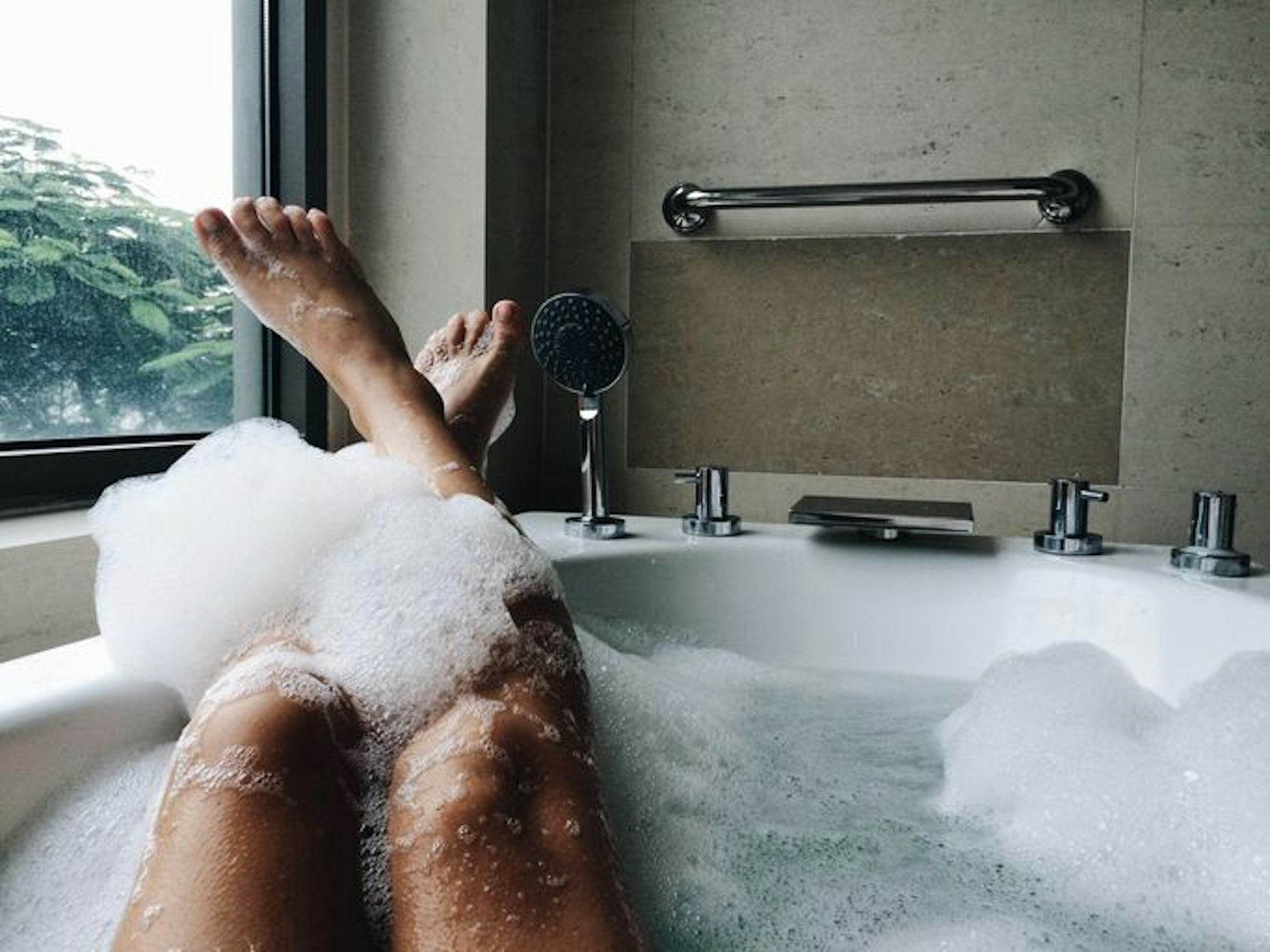 Frauenbeine ragen aus einer Badewanne bedeckt mit Badeschaum.