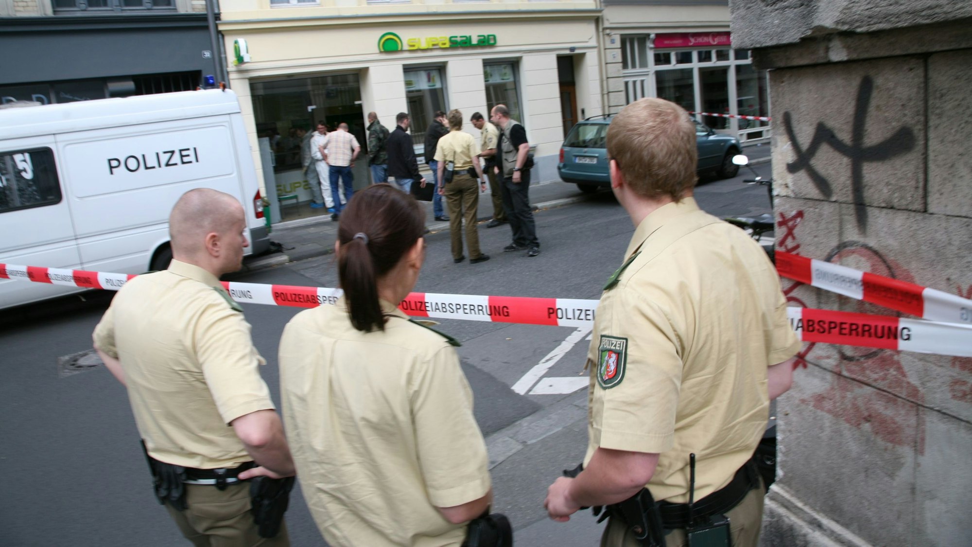 Drei Polizisten stehen hinter der Absperrung vor der Salatbar in der Gertrudenstraße in der Kölner Innenstadt, wo Anke Schäfer im Jahr 2007 ermordet wurde