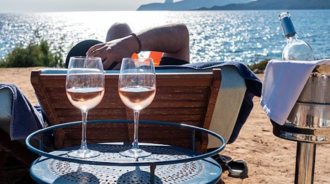 Ein sonniger Anblick! Während sich die Sonne auf dem Meer spiegelt, sorgen volle Weingläser für echtes Urlaubsfeeling. Die Aufnahme dient lediglich als Symbolfoto.