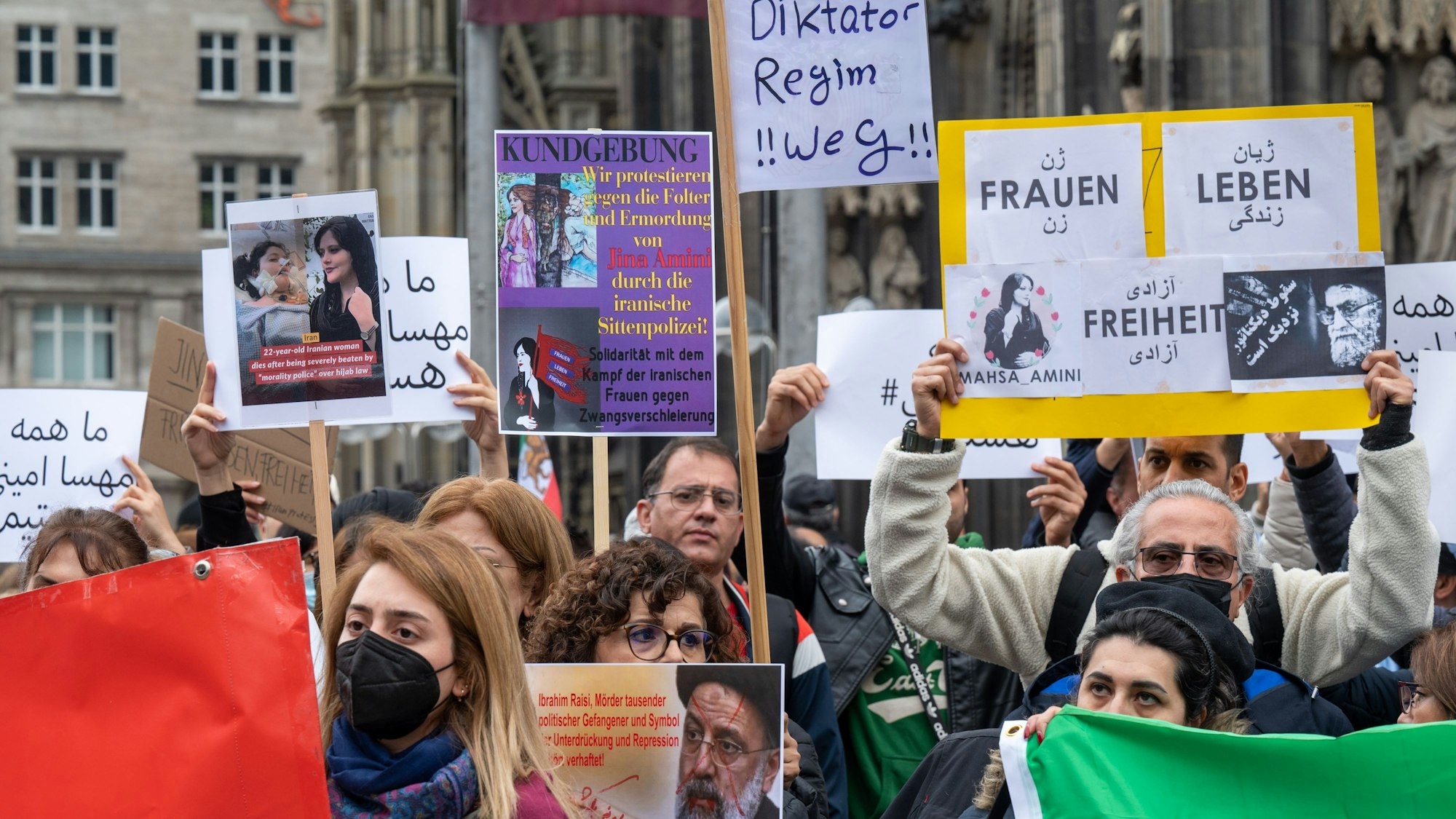 Iranerinnen und Iraner stehen mit Protest-Plakate vor dem Kölner Dom.