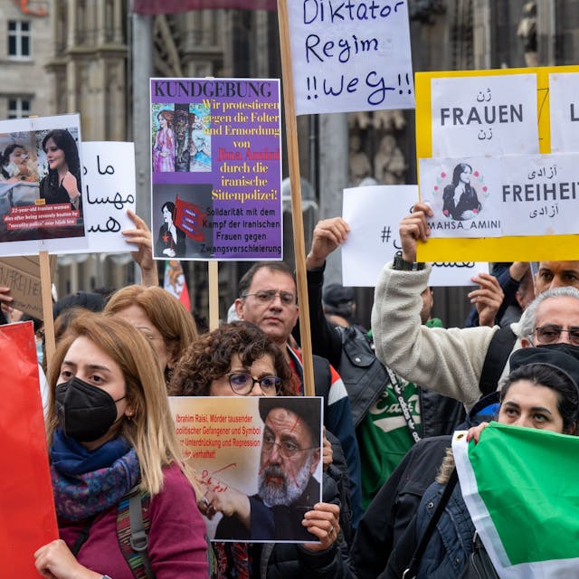 Iranerinnen und Iraner stehen mit Protest-Plakate vor dem Kölner Dom.&nbsp;
