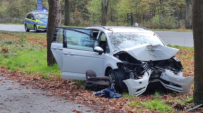 Ein Auto steht nach einem Baum-Aufprall stark beschädigt auf einem Grünstreifen.