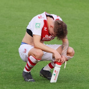 Simon Breuer kniet nach einem Spiel der U21 des 1. FC Köln enttäuscht auf dem Rasen.