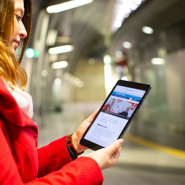 Eine junge Frau steht auf dem Bahnsteig und liest Nachrichten der Rundschau auf ihrem Tablet.