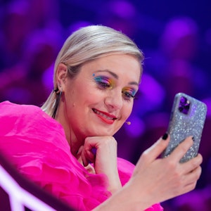 Ruth Moschner aus dem Rateteam sitzt am Ratepult im Finale der ProSieben-Show „The Masked Singer“ und blickt auf ihr Handy.