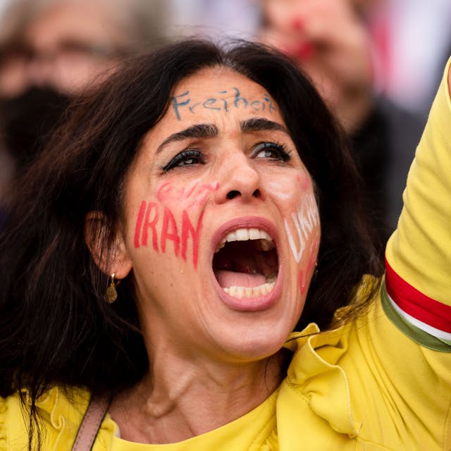 Eine Frau nahm am ·Marsch für die Freiheit·in Köln teil. Ihr Arm ist in die Luft gereckt, auf ihrer Wange steht „Iran“, auf der Stirn „Freiheit“.&nbsp;