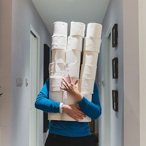 Person trägt viele Toilettenpapierrollen in den Armen und verdeckt ihr Gesicht. Bild für Amazon Toilettenpapier Artikel.