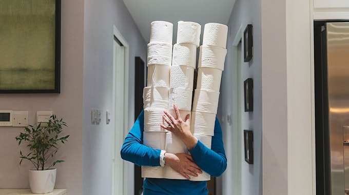 Person trägt viele Toilettenpapierrollen in den Armen und verdeckt ihr Gesicht. Bild für Amazon Toilettenpapier Artikel.