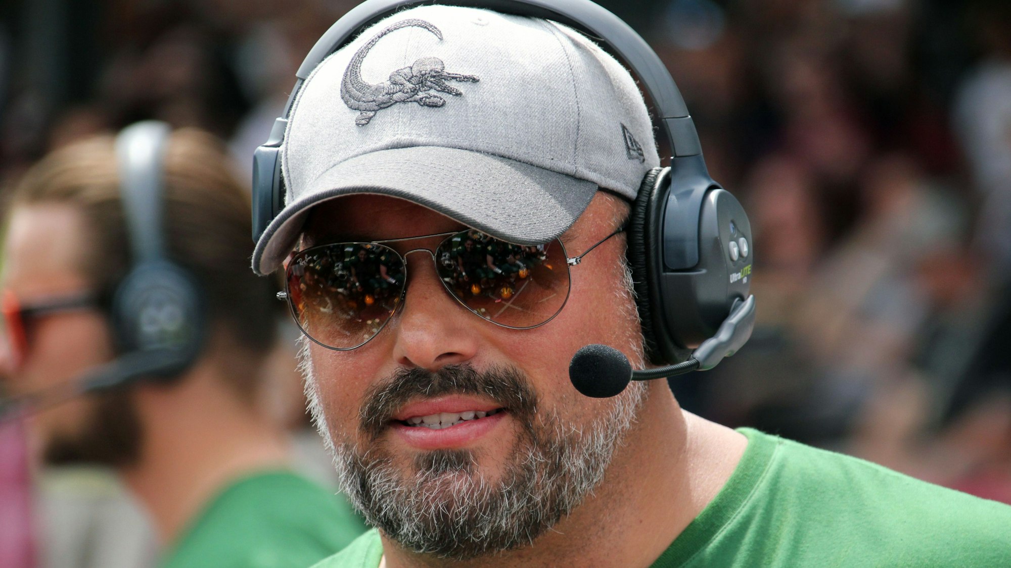 Ein Football-Trainer steht mit Kopfhörern, Sonnenbrille und Kappe am Spielfeldrand.