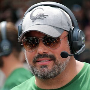 Ein Football-Trainer steht mit Kopfhörern, Sonnenbrille und Kappe am Spielfeldrand.