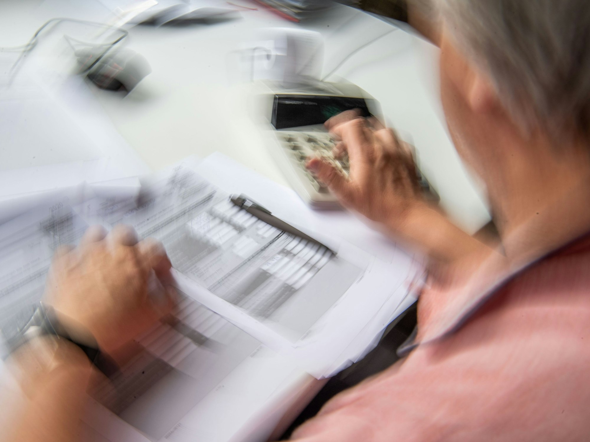 Ein Rentner füllt seine Steuererklärung aus und tippt zur Berechnung Zahlen in einen Tischrechner.