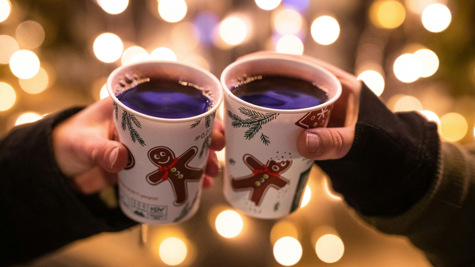 Zwei Menschen stoßen mit Glühwein in Bechern auf dem Weihnachtsmarkt an.