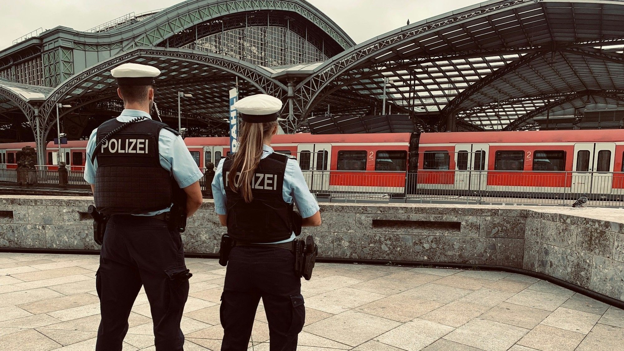 Die Bundespolizei am Hauptbahnhof Köln. Mit Schutzwesten bekleidet blicken die beiden Polizisten auf einen Zug im Bahnhof (Symbolbild).