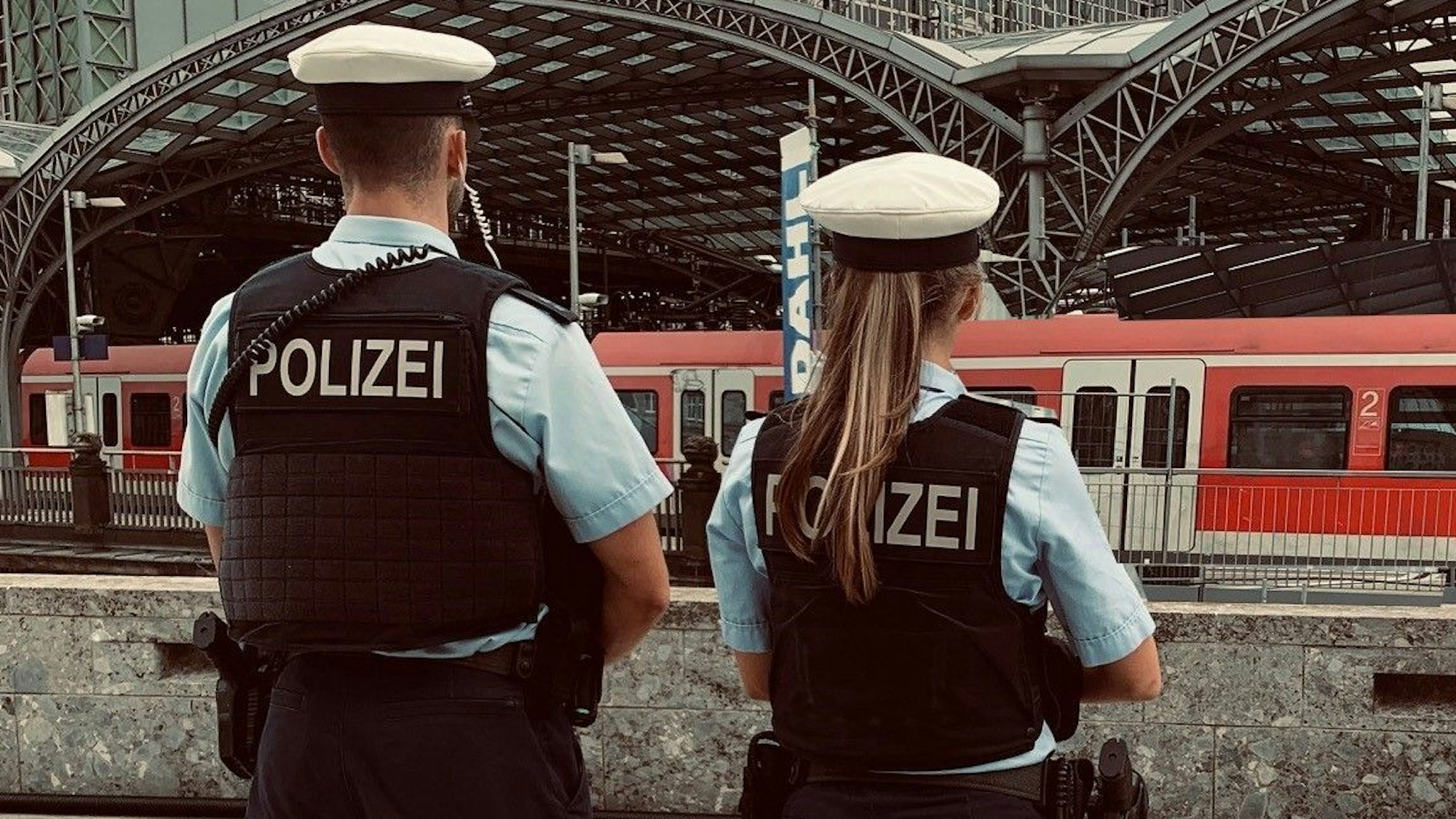 Zwei Beamte der Bundespolizei Köln stehen am Hauptbahnhof Köln und blicken auf die einfahrenden Züge.