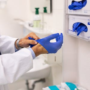 Ein Arzt zieht sich in der Praxis blaue Gummihandschuhe an.