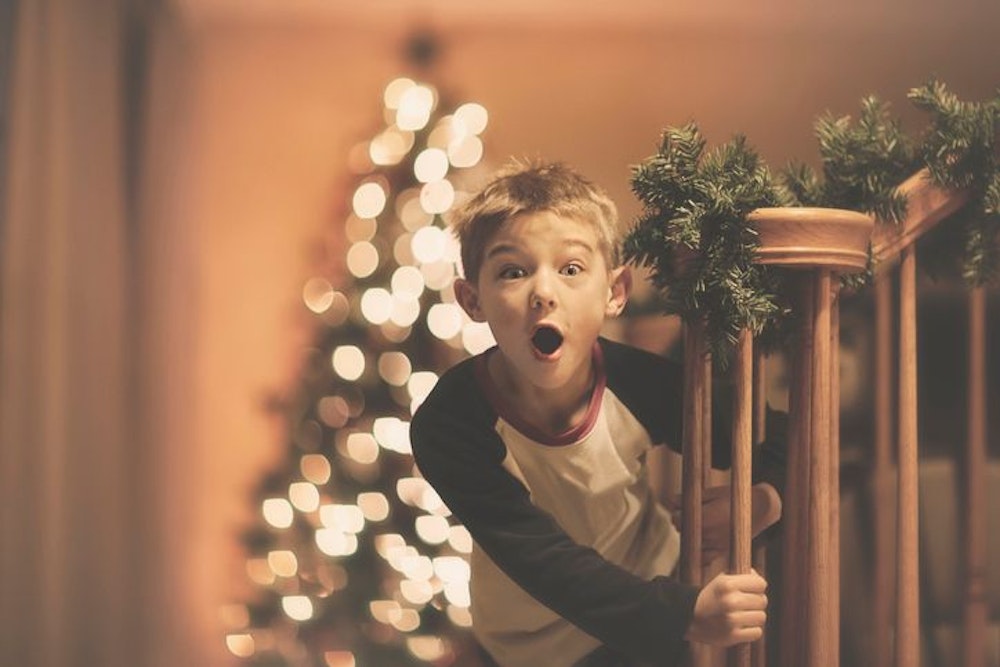 Ein Junge freut sich über seine Weihnachtsüberraschung. Im Hintergrund sieht man einen geschmückten Weihnachtsbaum. Bild für Shoppingwelt Adventskalender Sammelartikel für Kinder.