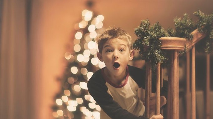 Ein Junge freut sich über seine Weihnachtsüberraschung. Im Hintergrund sieht man einen geschmückten Weihnachtsbaum. Bild für Shoppingwelt Adventskalender Sammelartikel für Kinder.