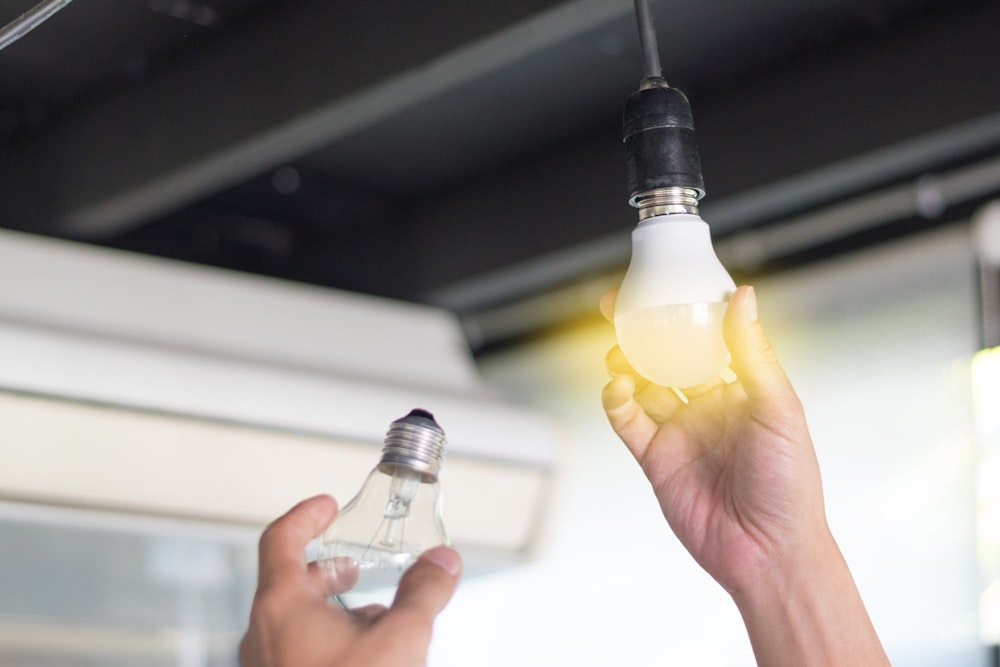 Person wechselt Glühbirne mit neuer LED Glühbirne. Bild für Amazon LED Lampen Artikel.
