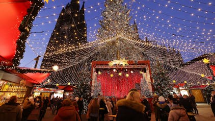 Besucher gehen über den Weihnachtsmarkt auf dem Roncalliplatz am Dom.
