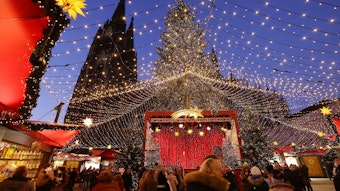 Besucher gehen über den Weihnachtsmarkt auf dem Roncalliplatz am Dom.