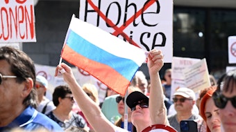 Eine Teilnehmerin einer pro-russischen Kundgebung hält eine russische Fahne hoch, andere Schilder auf denen durchgestrichene Panzer und die Worte "Keine Sanktionen" stehen.