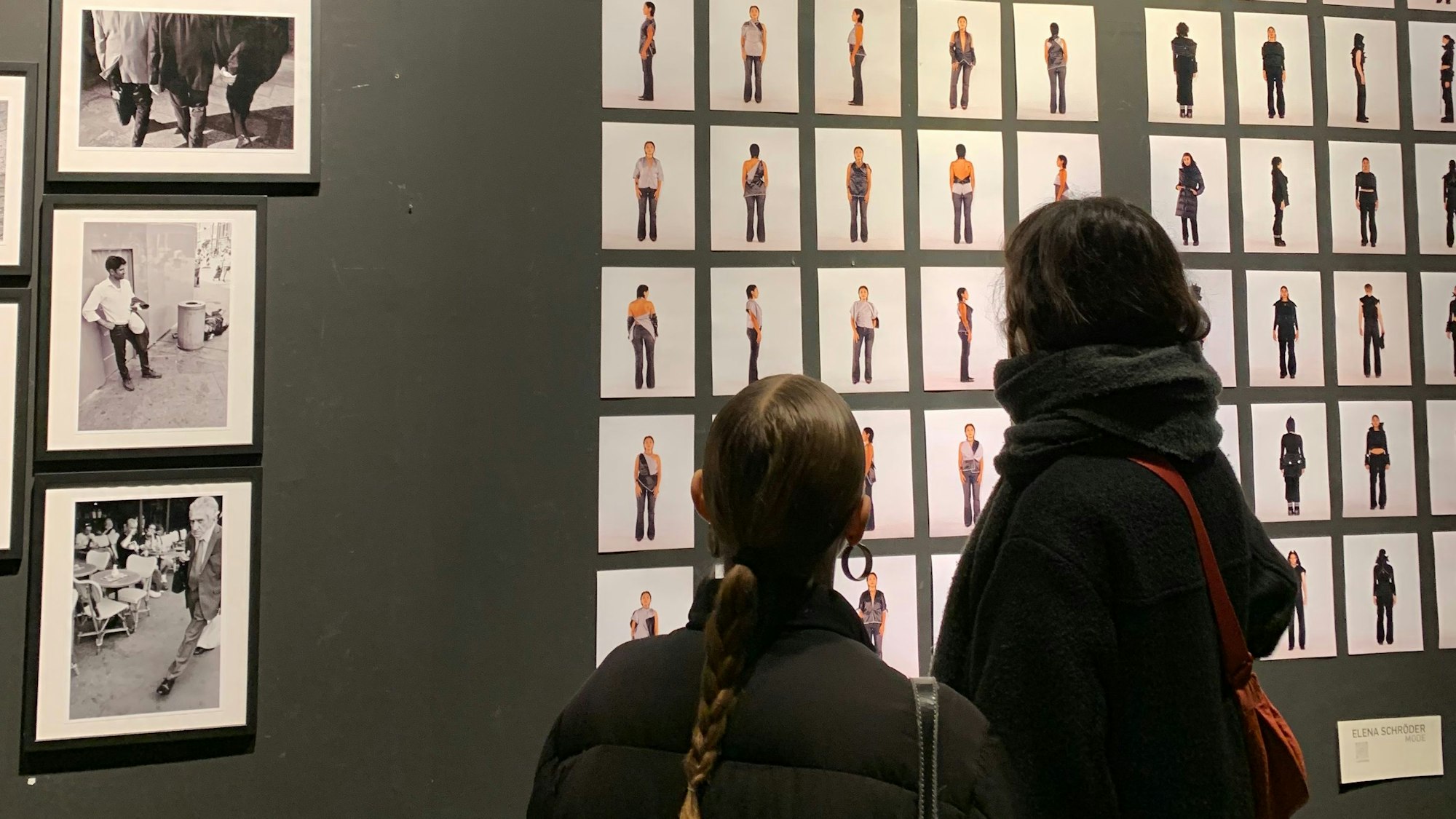 Zwei Besucherinnen betrachten eine große Anzahl an Bildern, die dichtgedrängt auf einer dunklen Wand angebracht sind in der Arty Farty Gallery.