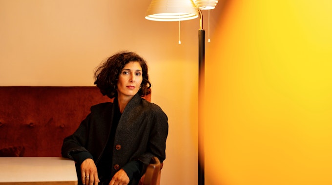 Nava Ebrahimi sitzt auf einem roten Sofa vor einer Stehlampe