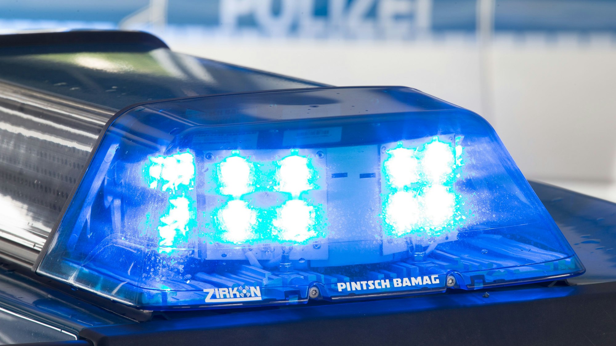Ein Blaulicht leuchtet auf dem Dach eines Polizeiwagens. Im Hintergrund steht ein weiterer Streifenwagen.