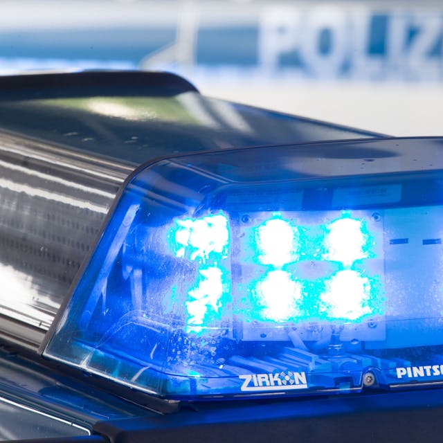 Eine Blaulicht leuchtet auf dem Dach eines Polizeiwagens. Im Hintergrund steht ein weiterer Streifenwagen.