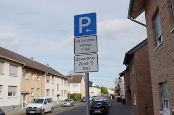 Ein Parken-Verkehrsschild steht auf einer Straße. Die Bewohner der Zone D können kostenfrei parken. Mehrere Autos stehen geparkt am Straßenrand.