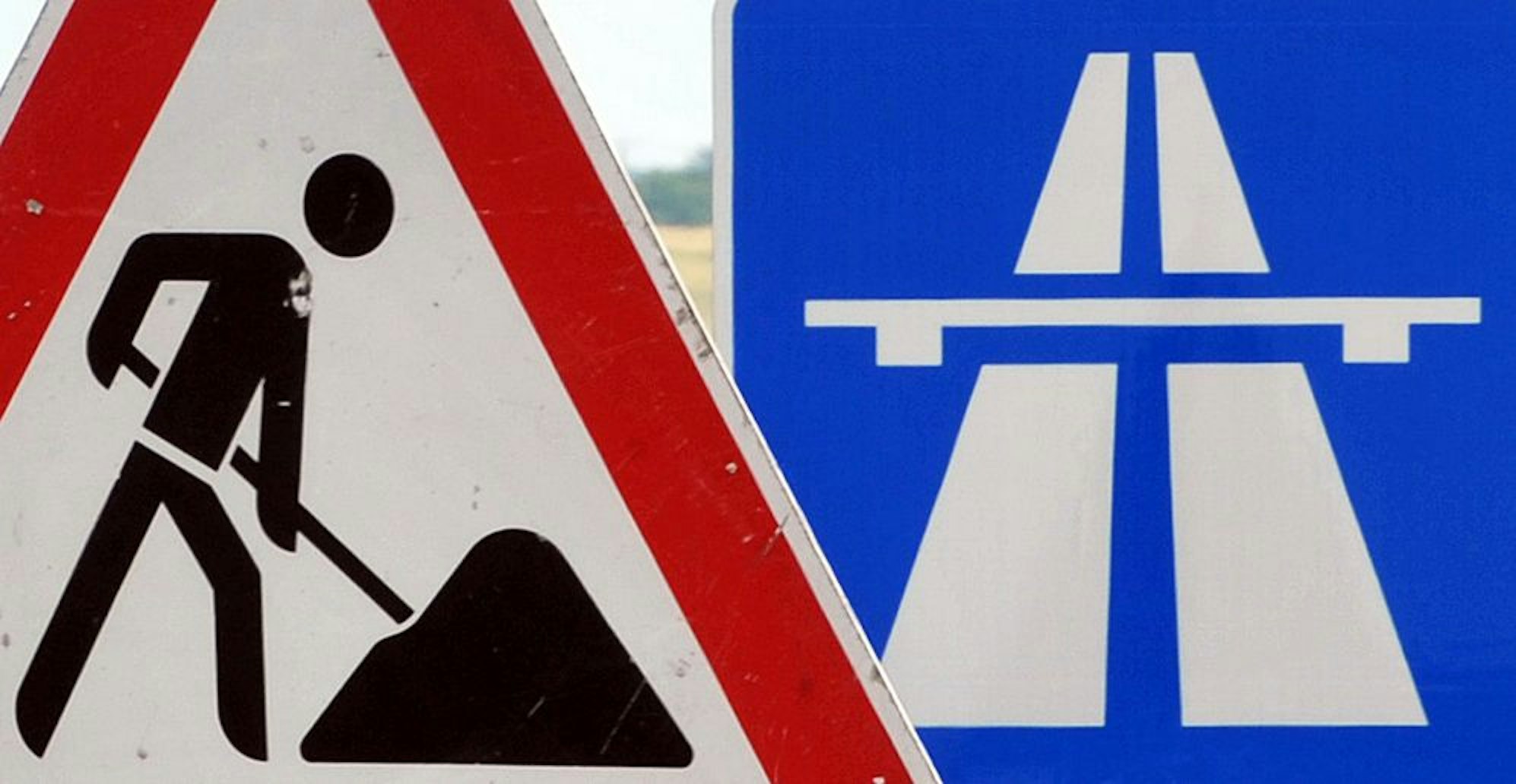 Ein Baustellenschild ist vor einem Autobahnschild platziert.