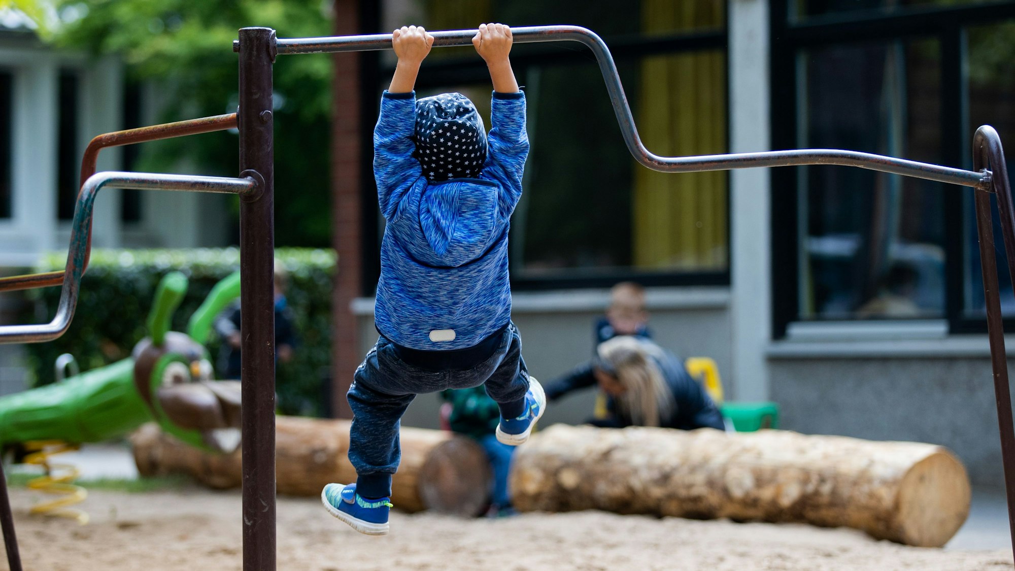 Ein Kind hängt am Klettergerüst auf einem Spielplatz, von hinten fotografiert.