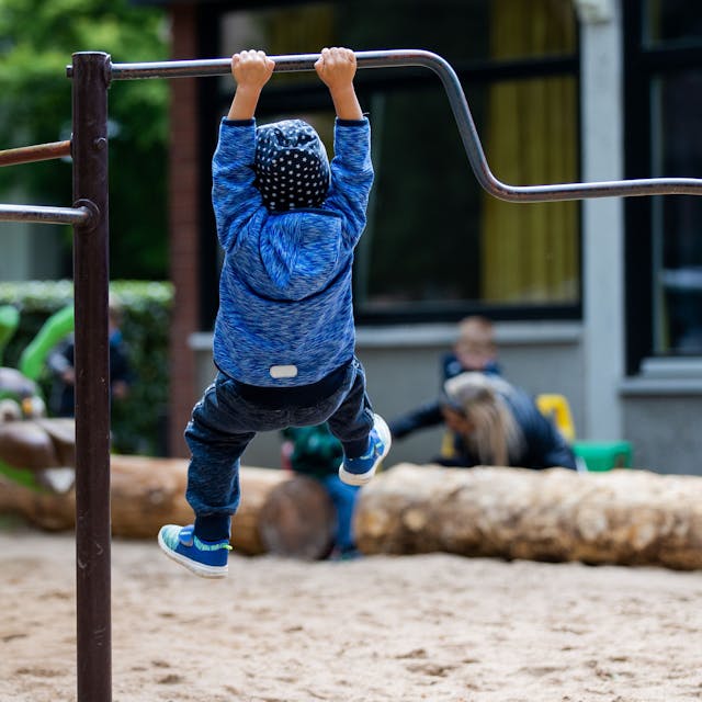 Ein Kind hängt am Klettergerüst auf einem Spielplatz, von hinten fotografiert.