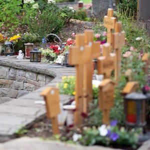 Auf Urnengräbern stehen kleine Holzkreuze, viele Blumen und Kerzen.