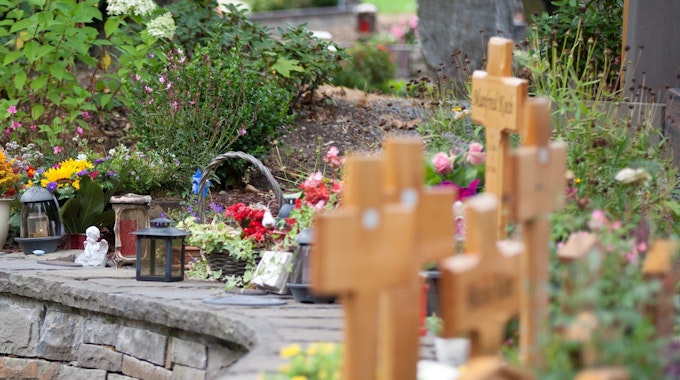 Auf Urnengräbern stehen kleine Holzkreuze, viele Blumen und Kerzen.