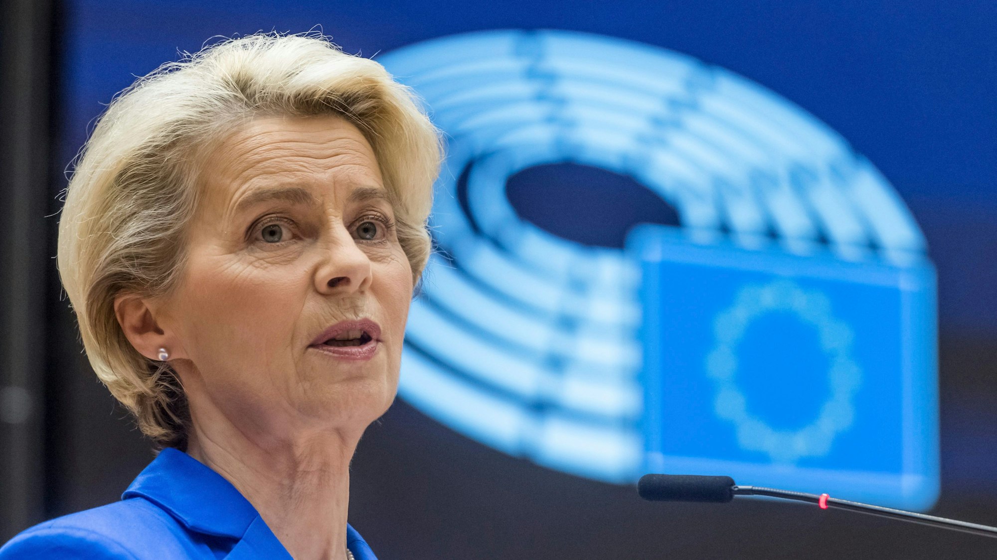 Ursula von Leyen im Europaparlament. Sie schaut ernst und hinter ihr ist die EU-Flagge zu sehen.