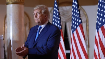 Ex-US-Präsident Donald Trump am Abend der Midterm-Wahlen in seiner Residenz in Mar-a-Lago. Trump steht vor drei US-amerikanischen Nationalflaggen und klatscht.