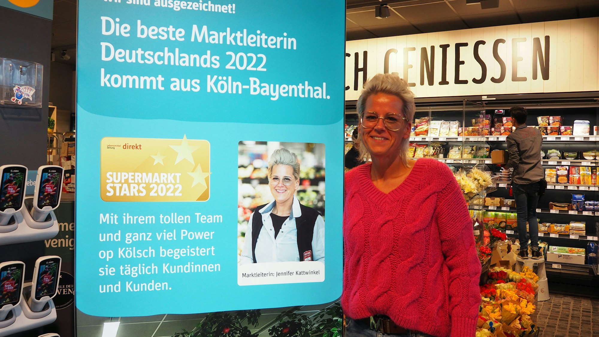 Jennifer Kattwinkel steht neben einem Porträt von sich selbst im Rewe-Markt in Köln-Bayenthal.