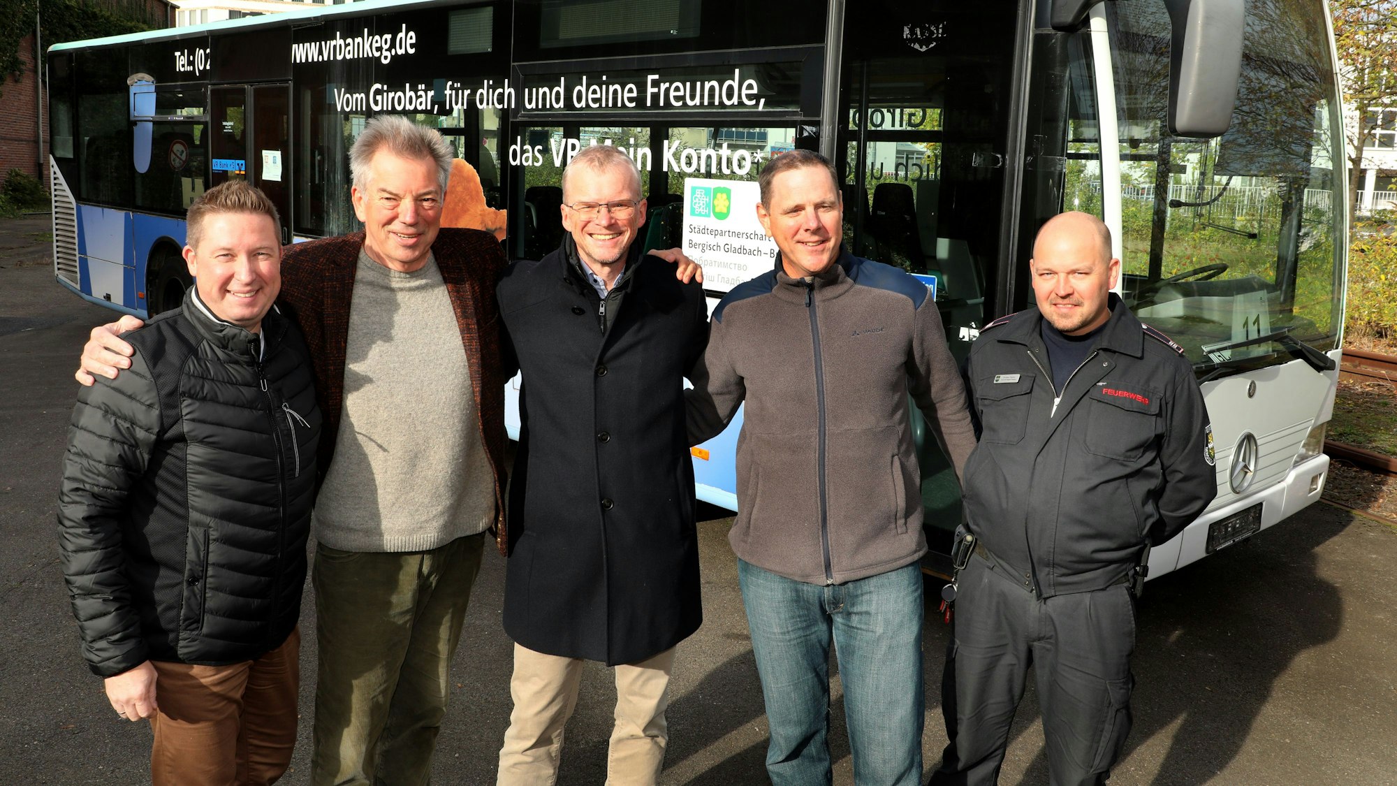Fünf beteiligte Männer der Städtepartnerschaft Bergisch Gladbach-Butscha stehen Arm in Arm vor einem Bus.