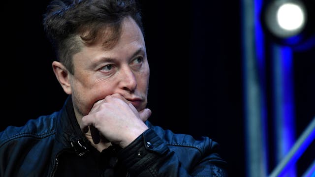 Elon Musk hält sich die Hand ans Kind und schaut nachdenklich.