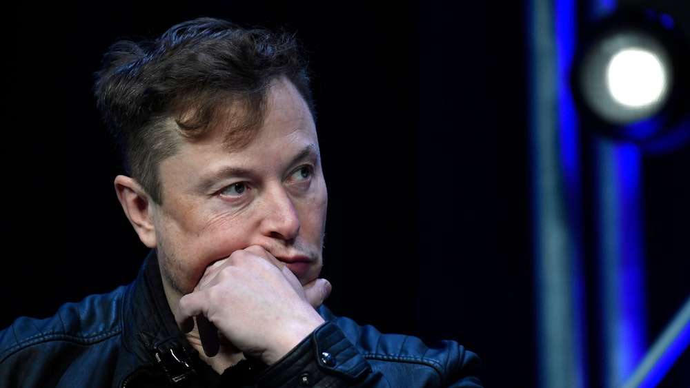 Elon Musk hält sich die Hand ans Kind und schaut nachdenklich.