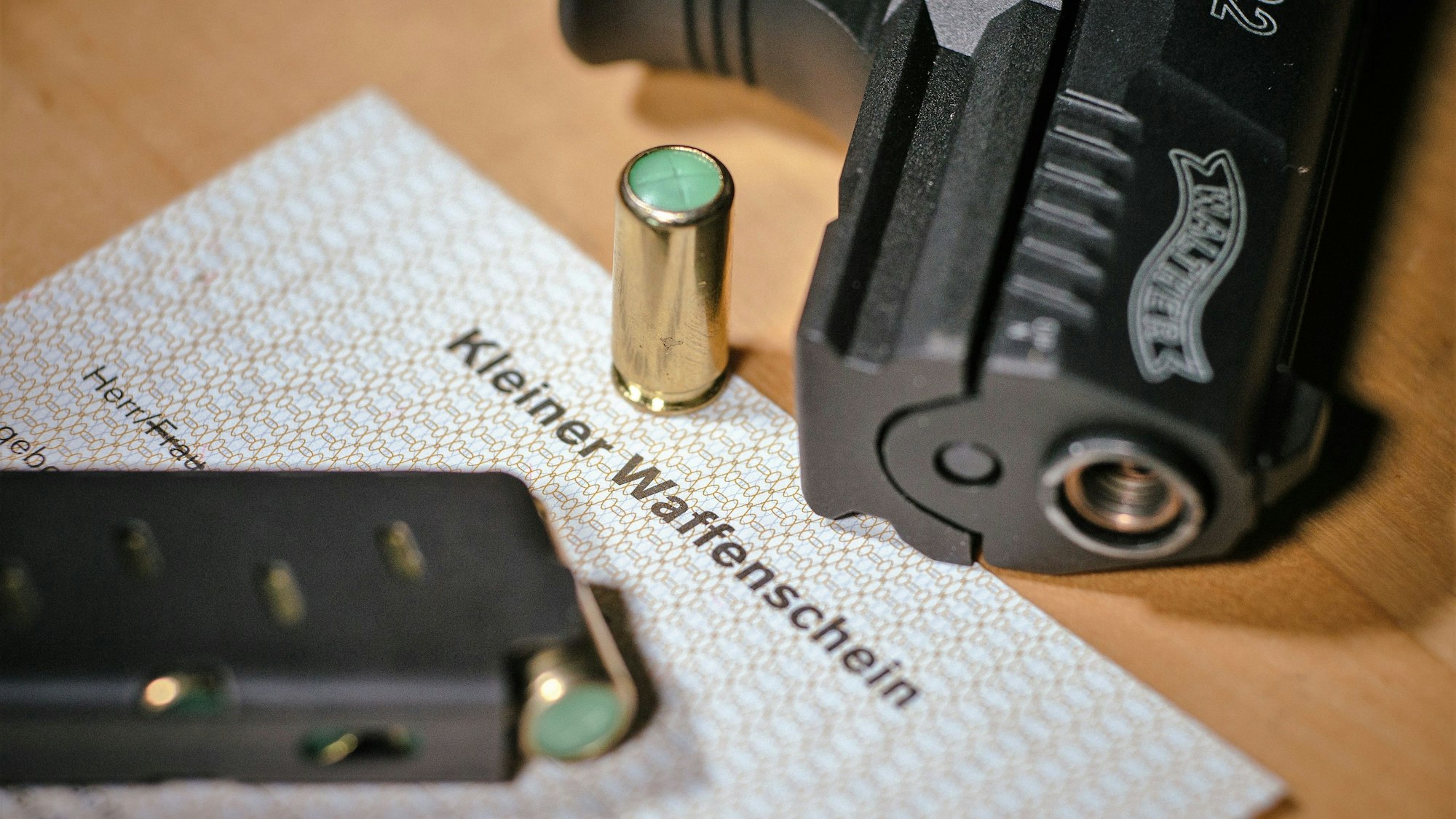 Ein Kleiner Waffenschein liegt zwischen einer Schreckschuss-Pistole, einem Magazin und einer Knallpatrone.