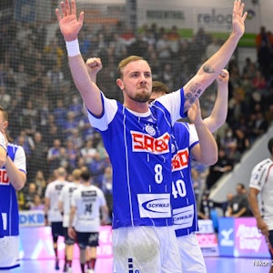 Handballspieler Lukas Blohme winkt den Zuschauern nach einem Spiel. Er trägt das blaue Trikot des VfL Gummersbach. Mannschaftskollegen stehen um ihn herum.