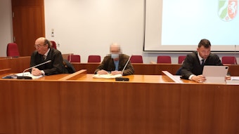 Der Angeklagte sitzt zwischen seinen Verteidigern auf der Anklagebank vor dem Landgericht Bonn.