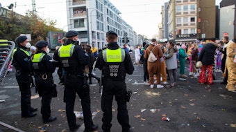 Junge Menschen feiern an der Zülpicher Strasse Karneval. Davor stehen Polizeibeamte und beobachten das Geschehen.