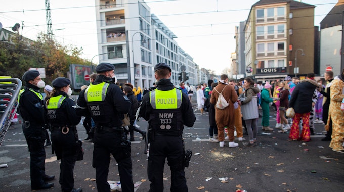 Junge Menschen feiern an der Zülpicher Strasse Karneval. Davor stehen Polizeibeamte und beobachten das Geschehen.